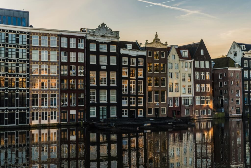 Scenic view of iconic canal houses in Amsterdam with reflections in the water during sunset.